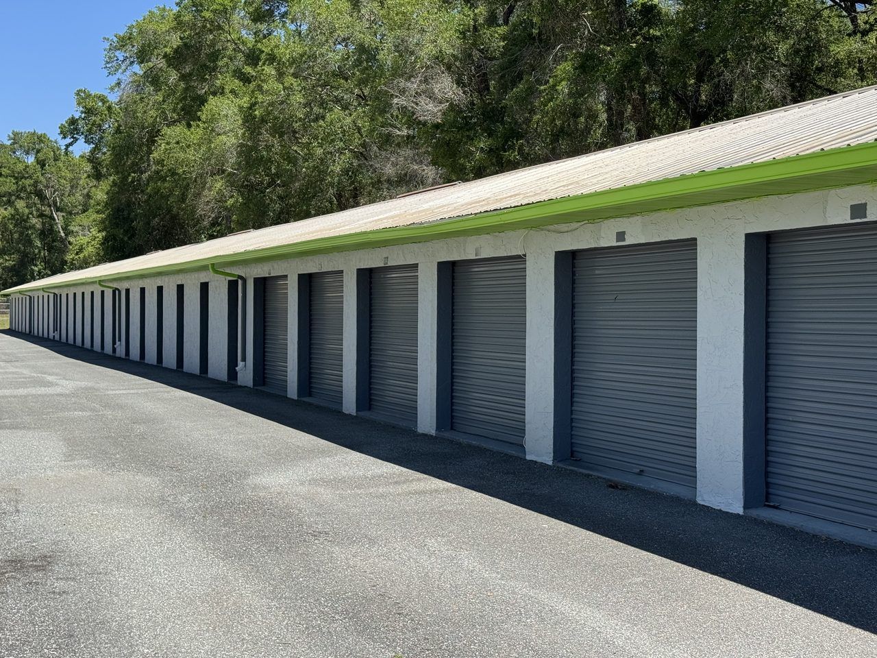 Row of drive-up storage units with grey roll-up doors and green trim at Cortez Self Storage, Brooksville, FL.