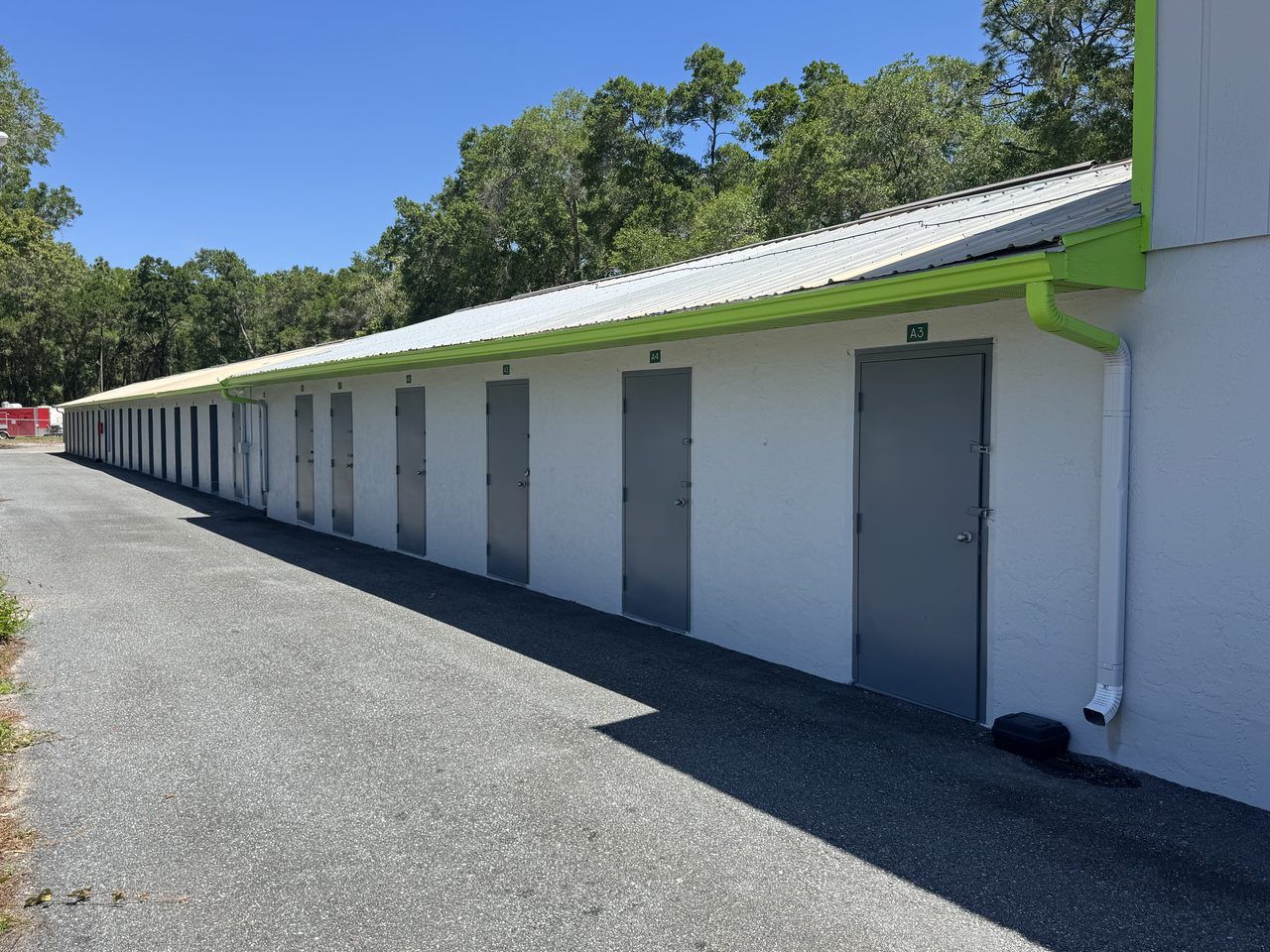 Row of secure walk-up storage doors with numbered units and green-trimmed eaves at Cortez Self Storage in Brooksville, Florida.